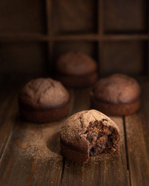 Çikolatalı ev yapımı kekler ve bir tanesi ısırılarak koparılmış. Koyu ahşap bir masada ev yapımı brovniler..