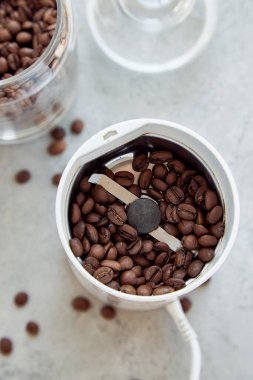 Kahve öğütücüsüyle ezilmiş kahve ve üzerinde kahve çekirdekleri olan cam bir kap.