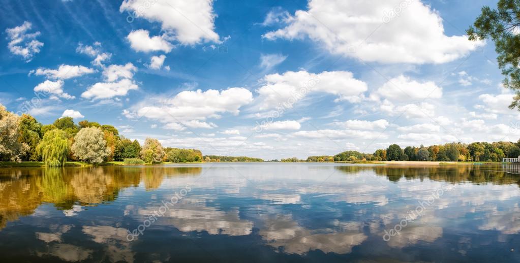 Autumn park, trees and blue sky reflected in water