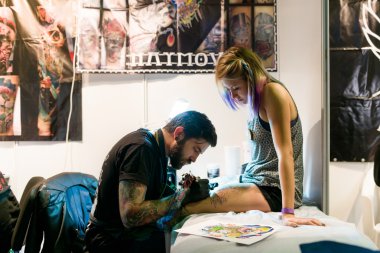 MINSK, BELARUS - SEPTEMBER 19, 2015: Professional tattoo artist doing tattoo on woman leg.