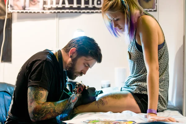 MINSK, BELARUS - SEPTEMBER 19, 2015: Professional tattoo artist doing tattoo on woman leg. — Stock Photo, Image