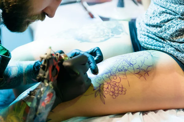 MINSK, BELARUS - SEPTEMBER 19, 2015: Professional tattoo artist doing tattoo on woman leg. — Stock Photo, Image