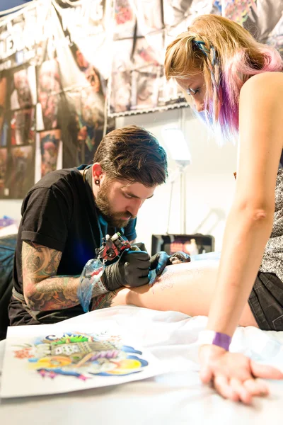 MINSK, BELARUS - SEPTEMBER 19, 2015: Professional tattoo artist doing tattoo on woman leg. 스톡 사진