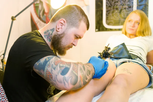 MINSK, BELARUS - SEPTEMBER 19, 2015: Professional tattoo artist doing tattoo on woman leg. — Stock Fotó