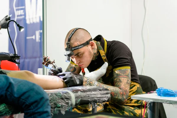 MINSK, BELARUS - SEPTEMBER 19, 2015: Professional tattoo artist doing tattoo on leg. 로열티 프리 스톡 사진