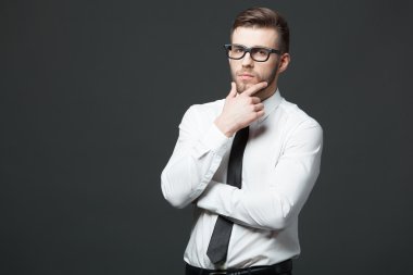 Young handsome businessman thinking on dark gray background.