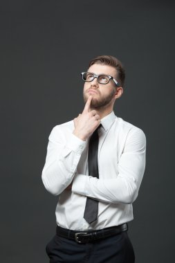 Young handsome businessman thinking on dark gray background.