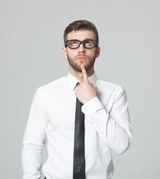 Jonge knappe zakenman denkt op een grijze achtergrond. — Stockfoto