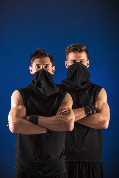 Dos bailarines masculinos posando en trajes ninja contra fondo azul — Foto de Stock