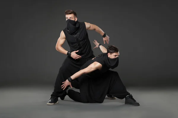 Two male dancers posing in ninja costumes on dark gray backgroun — Stock Photo, Image