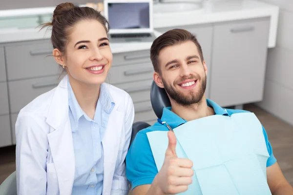 Jovem feliz na cadeira do dentista dando um polegar para cima . — Fotografia de Stock