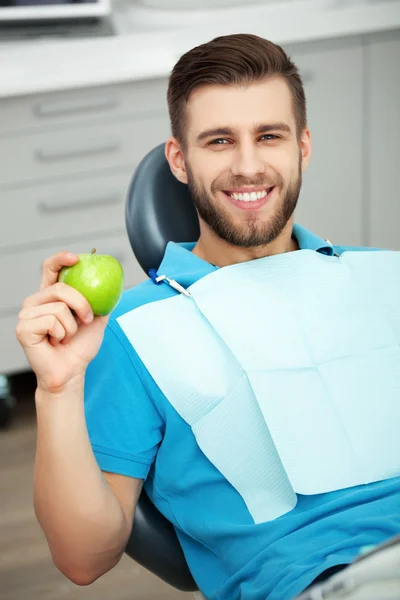 Retrato de paciente feliz em cadeira dental com maçã verde . — Fotografia de Stock