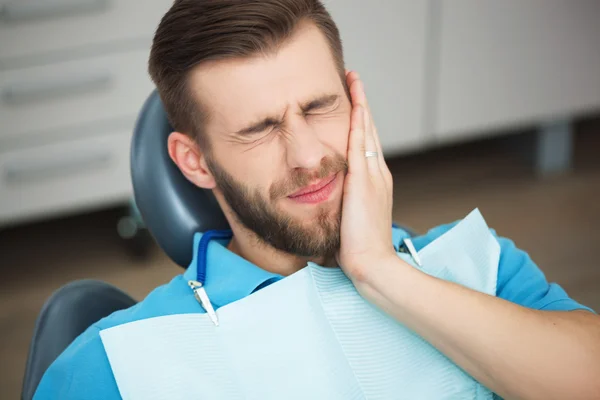 Retrato de homem jovem com dor de dente sentado no cha de um dentista — Fotografia de Stock