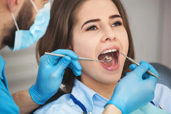 Młoda kobieta wychodzi jej zębów przez dentystę. — Zdjęcie stockowe