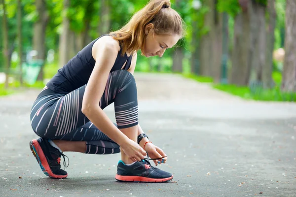 Schöne junge Frau bindet ihre Schnürsenkel vor einem Lauf. — Stockfoto