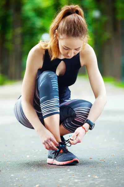 Schöne junge Frau bindet ihre Schnürsenkel vor einem Lauf. — Stockfoto