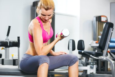 Spor salonunda dambıllarla egzersiz yapan genç bir kadın..