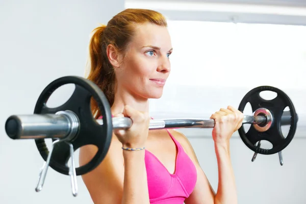 Junge Frau trainiert mit Langhantel im Fitnessstudio. — Stockfoto