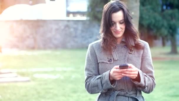 Приваблива бізнес-леді, використовуючи свій смартфон, що виходить на вулицю в історичному селі — стокове відео