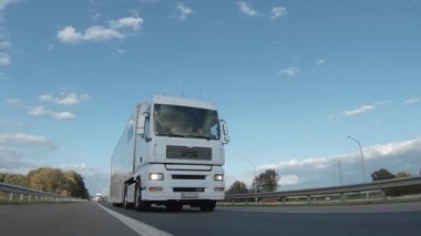Kargo kamyonu ve kargo karavanı bir otoyolda gidiyor. Beyaz Kamyon sabahın erken saatlerinde mal teslim ediyor. Çok düşük açılı bir araç. Yakın çekim sırasında..