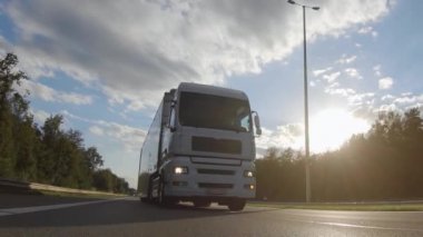 Kargo kamyonu ve kargo karavanı bir otoyolda gidiyor. Beyaz Kamyon sabahın erken saatlerinde mal teslim ediyor. Çok düşük açılı bir araç. Yakın çekim sırasında..