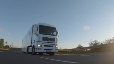 Kargo kamyonu ve kargo karavanı bir otoyolda gidiyor. Beyaz Kamyon sabahın erken saatlerinde mal teslim ediyor. Çok düşük açılı bir araç. Yakın çekim sırasında..