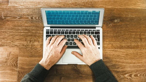 Man uses laptop on a wooden desk — Stock Photo, Image