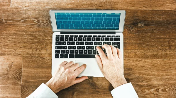 Homem usa laptop em uma mesa de madeira — Fotografia de Stock