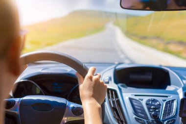 Girl hands on the steering wheel of a car while driving. Against the background, the windshield and road. Focus on her hand.