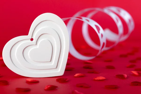 White heart with ribbon and red hearts on red — Stock Photo, Image