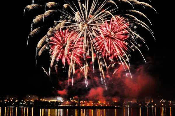 Fogos de artifício sobre a cidade à noite com reflexão na água — Fotografia de Stock