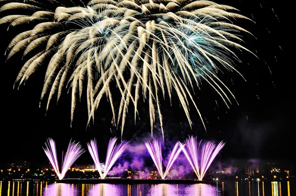 Fogos de artifício sobre a cidade à noite com reflexão na água — Fotografia de Stock