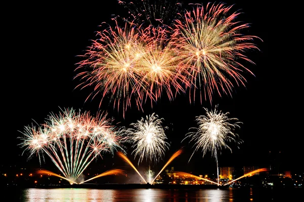 Vuurwerk over stad bij nacht met weerspiegeling in water — Stockfoto