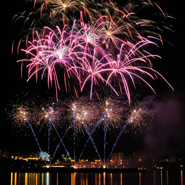 Fogos de artifício sobre a cidade à noite com reflexão na água — Fotografia de Stock