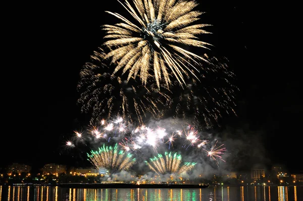 Fuochi d'artificio sulla città di notte con riflesso in acqua — Foto Stock