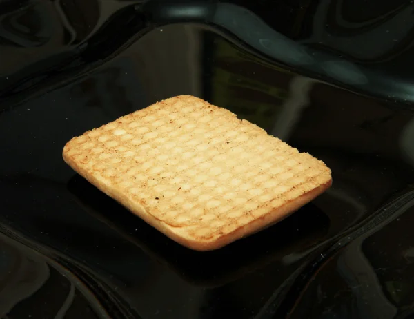 One cookie laying on the black plate — Stock Photo, Image