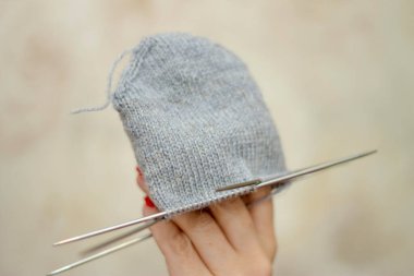 Kadın gri bir yün çorap örüyor ve hafif arka planda izole edilmiş parmaklarda tutuyor.