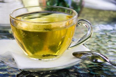 Açık havada şeffaf fincanda bir fincan bitki çayı ve yakınında da metal kaşık. Dağlık bölgelerdeki otlardan çay