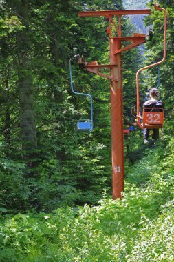 People going down on the double chairs of cableway through the forest. Dombai mountains, Russian Federation 10 june 2012