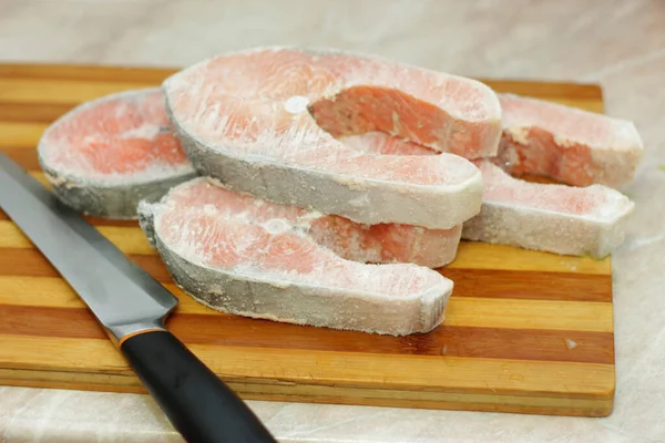 Frozen salmon raw red fish steak on the cooking table in the kitchen and knife laying near