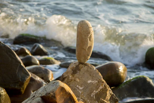 Balanced stone on the seashore summertime and sea waves background closeup on the sunset