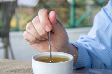 Kadın beyaz fincanda bir fincan bitkisel çaya şeker ekliyor ve açık havada karıştırıyor. Dağlık bölgelerdeki otlardan çay