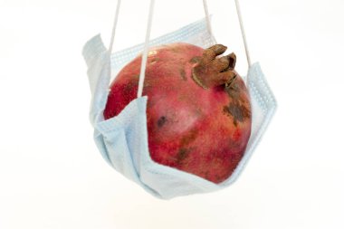 Beyaz arka planda izole edilmiş koruyucu bir tıbbi maskenin içinde asılı kırmızı bir nar. Coronavirus koruma kavramı