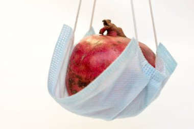 Bir kırmızı nar, beyaz arka planda izole edilmiş koruyucu bir tıbbi maskenin içinde yatıyor. Coronavirus koruma kavramı