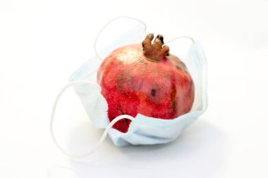 Bir kırmızı nar, beyaz arka planda izole edilmiş koruyucu bir tıbbi maskenin içinde yatıyor. Coronavirus koruma kavramı