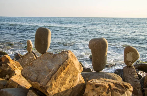 Yaz ve deniz dalgaları arka planında dengeli taşlar.