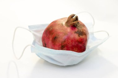 Bir kırmızı nar, beyaz arka planda izole edilmiş koruyucu bir tıbbi maskenin içinde yatıyor. Coronavirus koruma kavramı