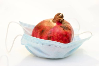 Bir kırmızı nar, beyaz arka planda izole edilmiş koruyucu bir tıbbi maskenin içinde yatıyor. Coronavirus koruma kavramı