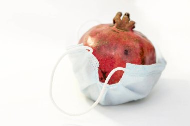 Bir kırmızı nar, beyaz arka planda izole edilmiş koruyucu bir tıbbi maskenin içinde yatıyor. Coronavirus koruma kavramı
