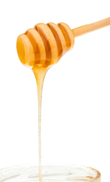 Honey flows down from wooden stick to glass jar — Stock Photo, Image